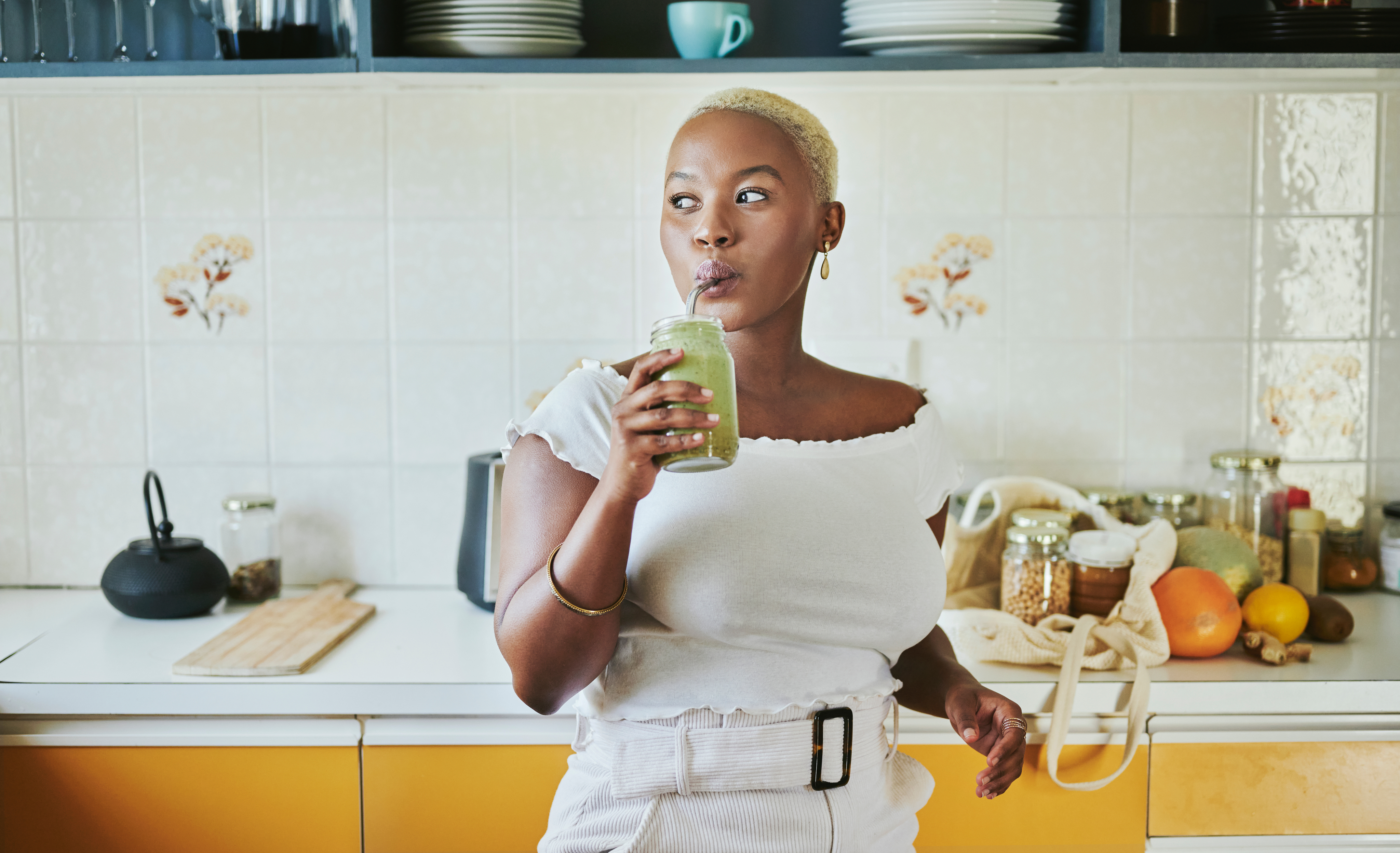 A woman in her kitchen enjoying a fruity drink through a straw