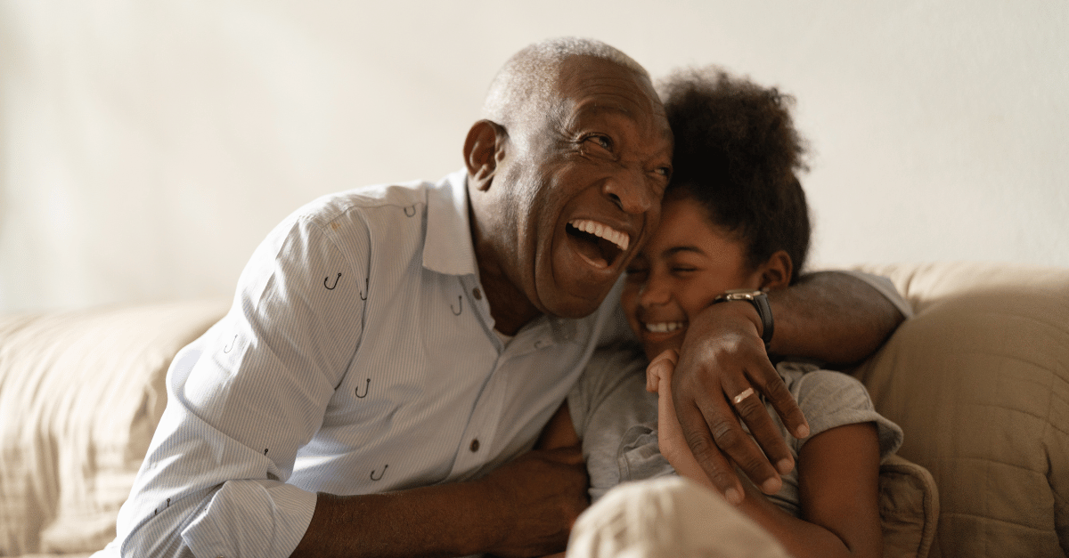 Grandfather hugging and laughing with granddaughter on the couch